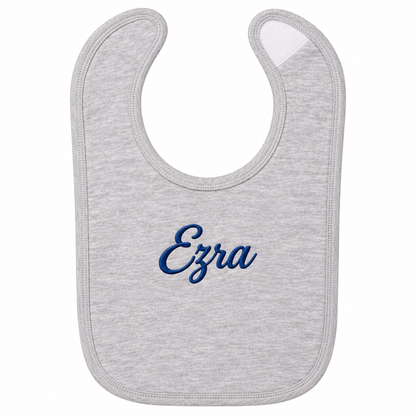 A light heather gray baby bib with the name 'Ezra' embroidered in dark blue cursive script in the center, shown on a plain white background.

