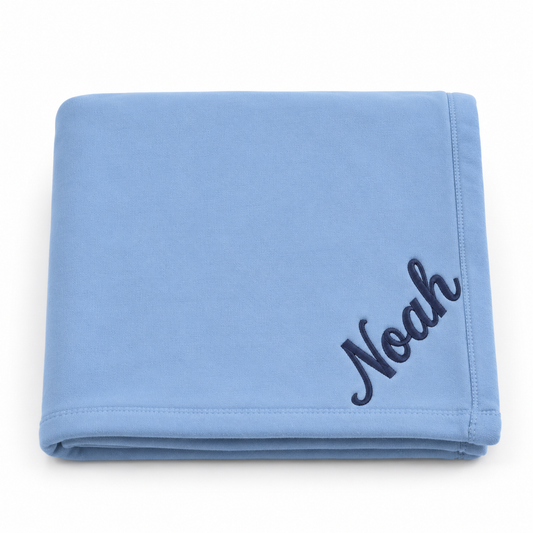 A folded light blue blanket with the name 'Noah' embroidered in dark navy script in the bottom right corner, set against a plain white background.

