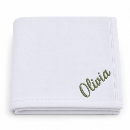 A folded white baby blanket with the name 'Olivia' embroidered in olive green script in the bottom right corner, set against a plain white background.

