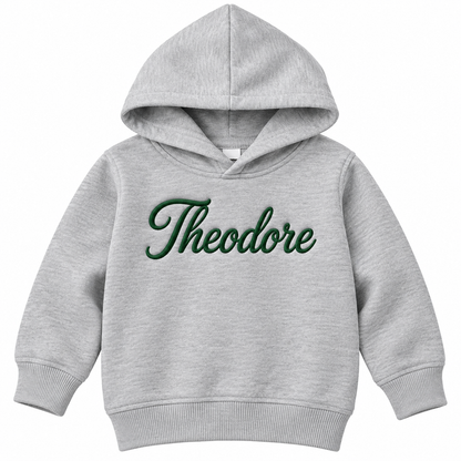 A light heather gray toddler pullover hoodie with the name 'Theodore' embroidered in dark green cursive script across the chest, shown on a plain white background.


