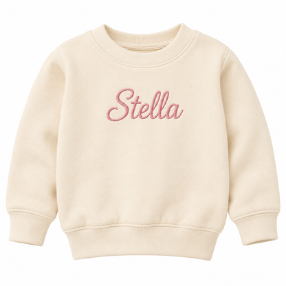 A cream-colored crewneck sweatshirt with the name 'Stella' embroidered in pink cursive across the chest, displayed on a clean white background.

