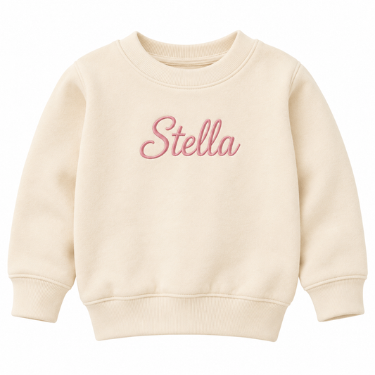 A cream-colored crewneck sweatshirt with the name 'Stella' embroidered in pink cursive across the chest, displayed on a clean white background.

